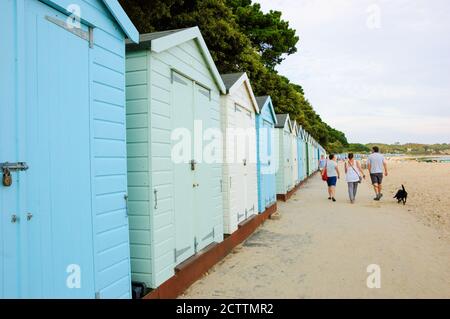 MUDEFORD, ENGLAND, UK - 26. AUGUST 2017: Menschen mit Hund wandern am Avon Beach mit seinen malerischen Holzhütten am Abend entlang. Stockfoto