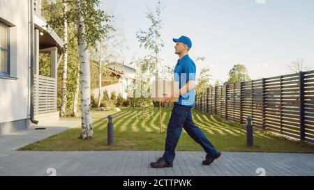 Delivery man Holding Card Board Paket tritt durch die Tore und geht zum Haus und klopft. Postpaket Wird Geliefert. Im Hintergrund Stockfoto