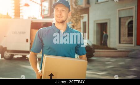 Portrait of Delivery man hält Karton-Box-Paket steht in modernen stilvollen Business District mit Lieferwagen im Hintergrund. Lächelnder Courier An Stockfoto