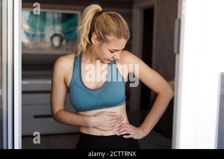 Nahaufnahme der Frau, die ihren Bauch hält. Schmerzen nach dem Training zu Hause. Gewichtsverlust, schlanker Körper, gesundes Konzept Stockfoto