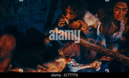 Nahaufnahme von Neandertaler oder Homo Sapiens Familie Kochen tierisches Fleisch über Lagerfeuer und dann essen. Stamm der prähistorischen Jäger-Sammler tragen Stockfoto