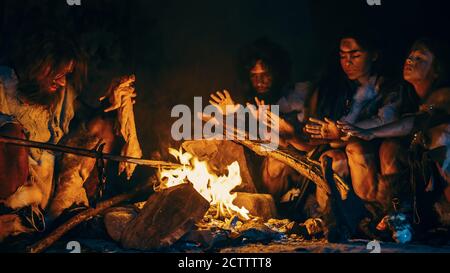 Neanderthal oder Homo Sapiens Familie Kochen tierisches Fleisch über Lagerfeuer und dann essen. Stamm der prähistorischen Jäger und Sammler mit Tierfelle Stockfoto