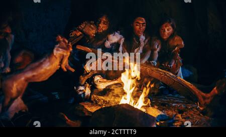 Neanderthal oder Homo Sapiens Familie Kochen tierisches Fleisch über Lagerfeuer und dann essen. Stamm der prähistorischen Jäger und Sammler mit Tierfelle Stockfoto