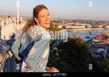 Junge unbeschwerte Stadtfrau, die in Sonnenuntergang lacht Stockfoto