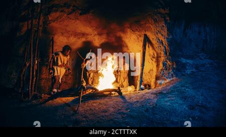 Stamm der prähistorischen Jäger und Sammler mit Tierfelle stehen um Bonfire außerhalb der Höhle in der Nacht. Porträt der Familie Homo Sapiens Stockfoto