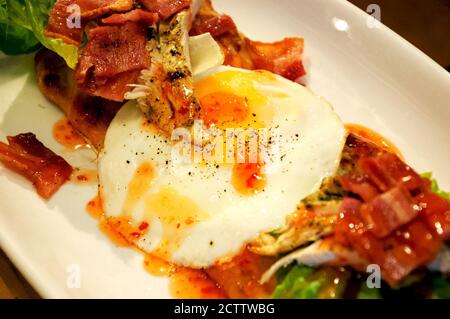 Englische Tapas im Frühstücksstil mit Spiegeleiern, Speck, gebratenen Hähnchenscheiben, grünem Salat und scharfer Chili-Pfeffer-Salsa auf geröstetem Fladenbrot. Stockfoto