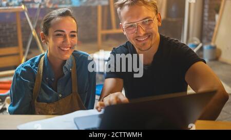 Einige Künstler sitzen in ihrem Studio verwenden Laptop-Computer, arbeiten an einem Projekt, reden und lächeln. Malerin und ihr Partner bei der Recherche Stockfoto