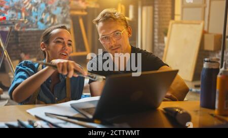 Einige Künstler sitzen in ihrem Studio verwenden Laptop-Computer, arbeiten an einem Projekt, reden und lächeln. Malerin und ihr Partner bei der Recherche Stockfoto