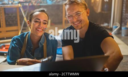 Einige Künstler sitzen in ihrem Studio verwenden Laptop-Computer, arbeiten an einem Projekt, reden und lächeln. Malerin und ihr Partner bei der Recherche Stockfoto
