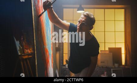 Talentierter Künstler arbeitet an abstrakter Malerei, verwendet Malpinsel, um erschreckend emotionale moderne Bild zu erstellen. Dark Creative Studio Große Leinwandständer Stockfoto