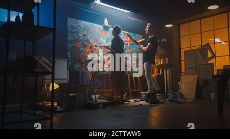 In der Kunstklasse: Talentierte junge Frau Künstler Farben mit einem Pinsel auf der großen Leinwand, ihr prominenter Mentor Maler lehrt sie über Technik und Stockfoto