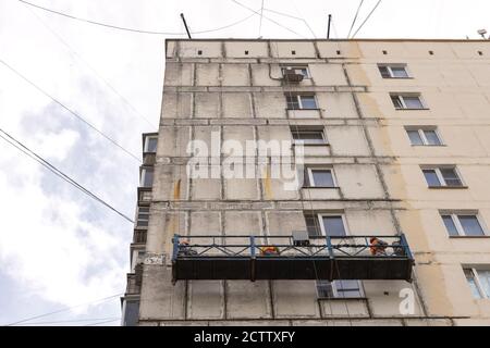 Renovierung der Fassade eines alten Gebäudes. Arbeiter in einer hängenden Baustation Stockfoto