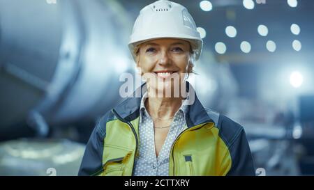 Portrait der professionellen Schwerindustrie weibliche Ingenieurin trägt Sicherheitsuniform und Harthut, lächelnd charmant. Im Hintergrund unfokussiert groß Stockfoto