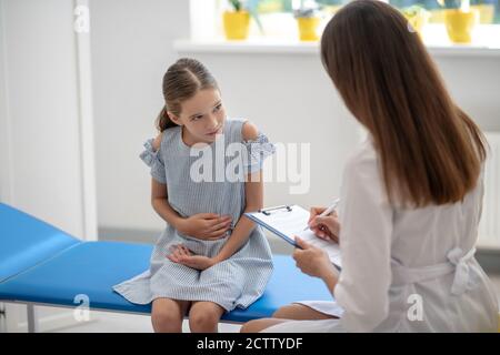 Mädchen mit Bauchschmerzen und im Gespräch mit dem Weibchen Arzt Stockfoto