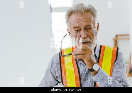 Ein älterer Arbeiter entfernte Brille wegen der Reizung der Augen oder des Stresses durch harte Arbeit. Stockfoto