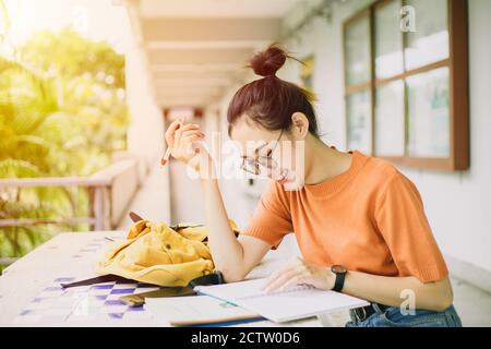 Eine junge Frau oder asiatische Universitätsstudentin Mädchen teen sitzen mit einem Lächeln, während Notizen auf einem Notizbuch oder genießen Sie Hausaufgaben auf dem Campus. Stockfoto