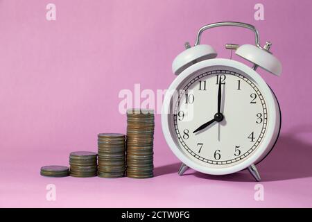 Münzstapel mit Wecker mit süßen rosa Raum Hintergrund für Zeiten, Geld zu sparen Konzept gestapelt. Stockfoto