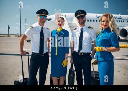 Fröhliche Fluglinienarbeiter, die vor dem Flug auf dem Flugplatz stehen Stockfoto