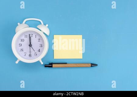 Weißer Wecker mit gelbem Schallplattenblatt, Stift auf blauem Hintergrund, Kopierplatz Stockfoto