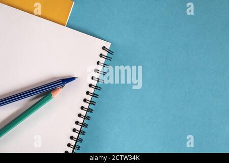 Unbeschriftete Spiralnotizheftchen mit weißer Seite und mehreren Bleistiften auf einem blauen Tisch. Stockfoto