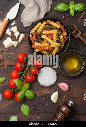 Fusilli Pasta in schwarzer Schüssel mit Parmesan-Käse und Tomaten, Öl und Knoblauch mit Basilikum und Leinentuch auf Holzhintergrund. Draufsicht Stockfoto