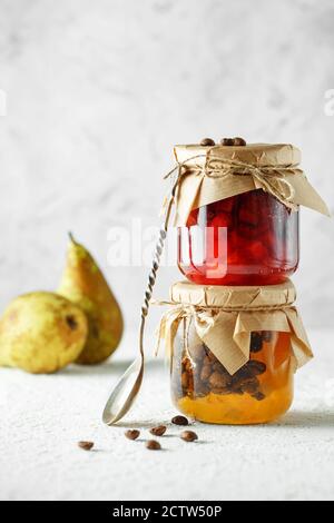 Zwei Gläser Obst hausgemachte Marmelade. Birne Marmelade mit Kaffeebohnen und Jar von Blutorange Marmelade auf hellgrauem Hintergrund. Stockfoto