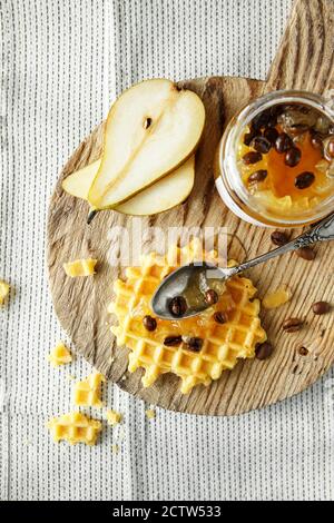 Flach-Lay mit Wiener Waffeln mit Birnenmarmelade mit Kaffeebohnen. Glas von Birne Marmelade auf Holz Schneidebrett auf Leinenhintergrund. Top-down Food Foto Stockfoto