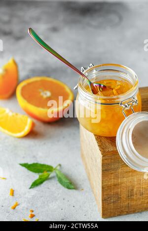 Hausgemachte Orangenmarmelade im Glas auf der Holzkiste auf dem grauen Hintergrund. Orangenmarmelade im Swing-Top-Glas auf Holz mit orangefarbenen Scheiben im Rücken. PH-wert für Lebensmittel Stockfoto