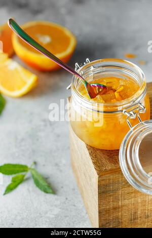 Hausgemachte Orangenmarmelade im Glas auf der Holzkiste auf dem grauen Hintergrund. Orangenmarmelade im Swing-Top-Glas auf Holz mit orangefarbenen Scheiben im Rücken. PH-wert für Lebensmittel Stockfoto