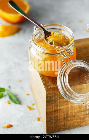 Hausgemachte Orangenmarmelade im Glas auf der Holzkiste auf dem grauen Hintergrund. Orangenmarmelade im Swing-Top-Glas auf Holz mit orangefarbenen Scheiben im Rücken. PH-wert für Lebensmittel Stockfoto