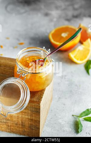 Hausgemachte Orangenmarmelade im Glas auf der Holzkiste auf dem grauen Hintergrund. Orangenmarmelade im Swing-Top-Glas auf Holz mit orangefarbenen Scheiben im Rücken. PH-wert für Lebensmittel Stockfoto