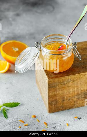 Hausgemachte Orangenmarmelade im Glas auf der Holzkiste auf dem grauen Hintergrund. Orangenmarmelade im Swing-Top-Glas auf Holz mit orangefarbenen Scheiben im Rücken. PH-wert für Lebensmittel Stockfoto