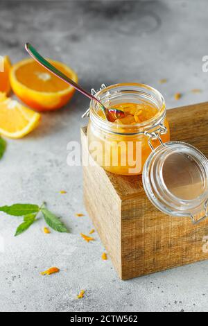 Hausgemachte Orangenmarmelade im Glas auf der Holzkiste auf dem grauen Hintergrund. Orangenmarmelade im Swing-Top-Glas auf Holz mit orangefarbenen Scheiben im Rücken. PH-wert für Lebensmittel Stockfoto