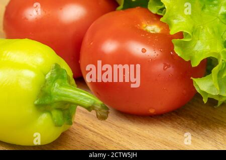 Schönes, saftiges Gemüse mit Wassertropfen Paprika, Tomaten, Salatblätter auf einem Holzbrett Nahaufnahme Stockfoto