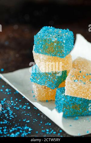 Hausgemachte gelbe und blaue Marmelade Süßigkeiten in zuckersüßem Sand auf dunklem Hintergrund. Fruchtgelee Süßigkeiten. Obst Kaubonbons. Jelly Bean. Sortiment an Stockfoto