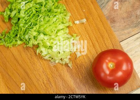 Geschnittene Salatblätter und eine ganze reife Tomate auf einem Holzbrett, Draufsicht, Kopierraum Stockfoto