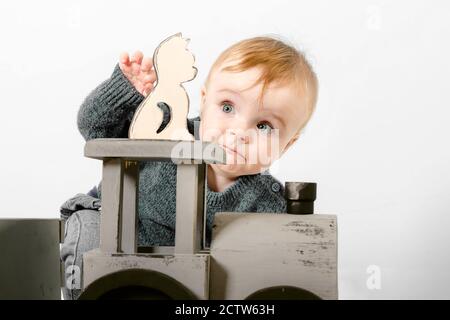 Überrascht ein Jahr altes Kind in einem grauen Pullover spielt Holzspielzeug. Blonde Baby Junge auf weißem Hintergrund. Nahaufnahme Stockfoto