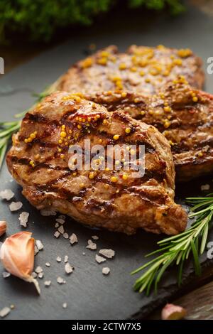 Gegrillte Rindersteaks mit Gewürzen. Fertiggerichte zum Abendessen auf dunklem Steingrund Stockfoto