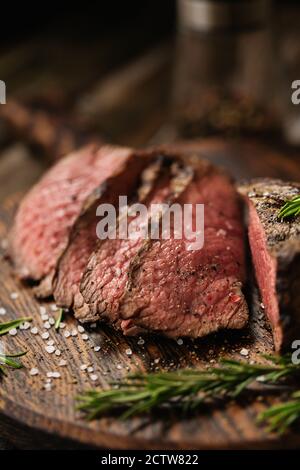 Saftig Medium Beef Rib Eye Steak Scheiben auf Holzbrett mit Kräutern Gewürze und Salz. Fertig zum Essen Steak mit Zutaten auf einem Schneidebrett. Stockfoto