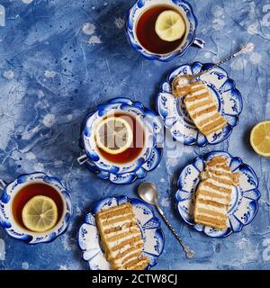 Urlaub Stillleben. Teller mit Stücken von leckeren Kuchen und Tassen Tee mit Zitrone auf grunge blauen Hintergrund. Flach Lay Nachmittag Kaffee Pause Tisch top s Stockfoto
