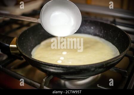 Der Pfannkuchenteig wird aus der Nähe aus einem Eimer in die Pfanne gegossen. Konzentrieren Sie sich auf die Schaufel mit dem Teig Stockfoto