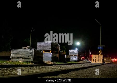 Pflasterplatten aus Naturstein liegen in einem Stapel auf einer Stadtstraße in der Nacht. Reparaturen zur Verbesserung der Straßen der Stadt Stockfoto