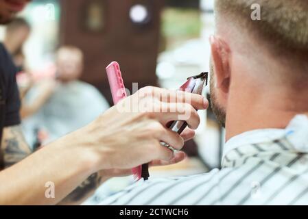 Nahaufnahme der Rückseite des Mannes im Friseurladen, der seinen Schnurrbart mit einem roten Trimmer schneiden ließ. Stockfoto