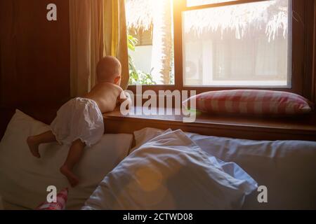 Ein kleines Kind schaut aus dem Fenster, während es auf dem Bett steht. Stockfoto