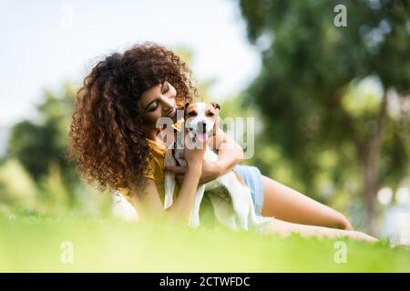 Selektiver Fokus der freudigen Frau umarmt Jack russell Terrier Hund Beim Liegen auf dem Rasen Stockfoto