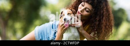 Horizontale Ausrichtung der lockigen Frau kuscheln Jack russell Terrier Hund Während der Ruhe im Park Stockfoto