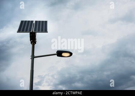 Sonnenkollektoren auf Straßenlaterne mit Licht an und wolkigen Himmel. Stockfoto