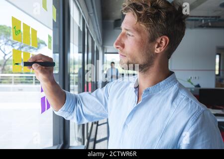 Smart lässig gekleidet kaukasischen Geschäftsmann schriftlich Memos auf Haftnotizen an einem Fenster geklebt. Kreative Business-Profi arbeiten in einem geschäftigen modernen Stockfoto