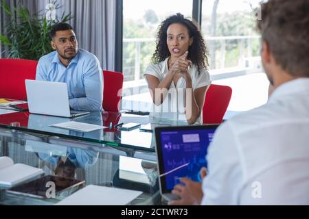Mixed-Race-Geschäftsfrau während einer Geschäftsbesprechung gestikuliert und gesprochen, ein gemischter männlicher Kollege sitzt neben ihrem Zuhören. Kreatives Geschäft Stockfoto