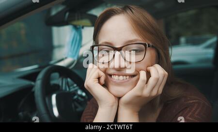 Nahaufnahme, Gesichtsausdruck einer jungen kaukasischen Frau, die auf dem Fahrersitz sitzt. Gesichtsmaske, die auf dem Spiegel hängt. Hochwertige Fotos Stockfoto